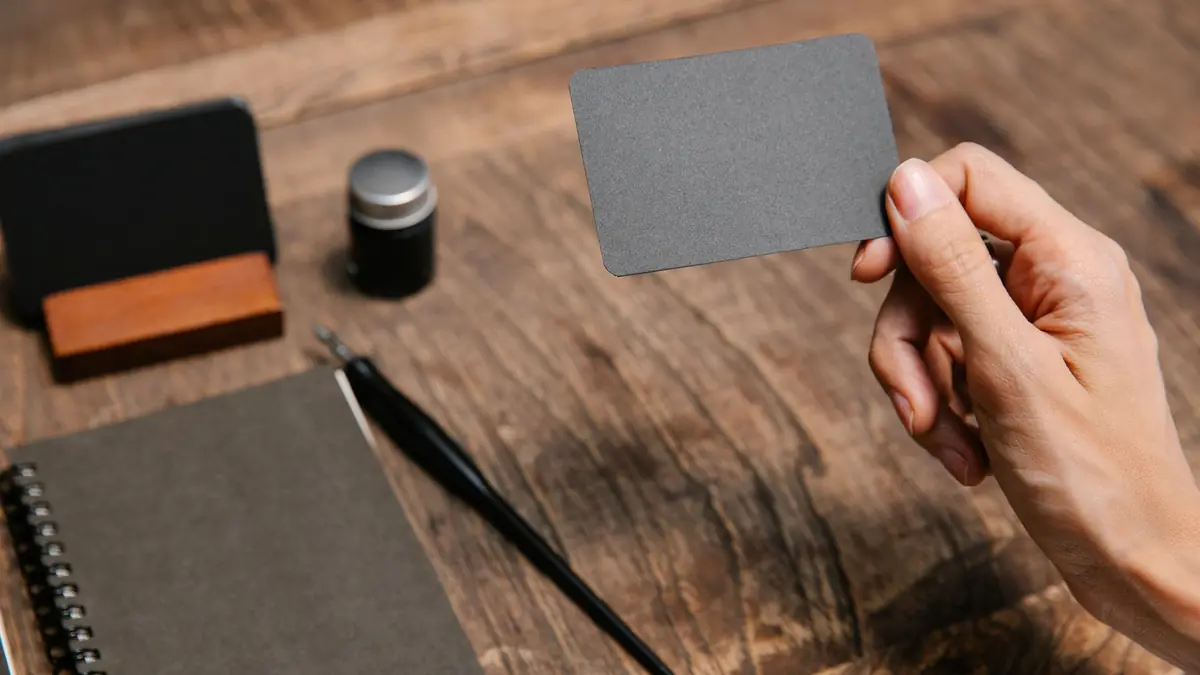 A close-up of a hand holding a blank business card above a wooden desk with office, illustrating med spa branding